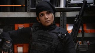 Halle Berry sits dressed in tactical gear with a serious expression next to some weapons in The Union.