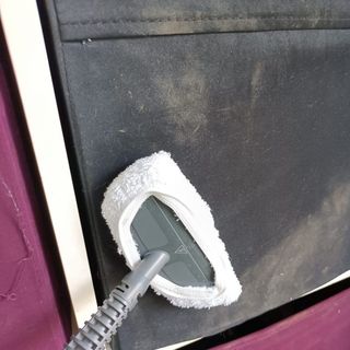 Closeup of a hoover steam cleaner with mop head removing dirt from upholstered furniture