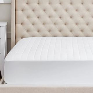 Boll & Branch Organic Mattress Protector on a beige bed frame. 