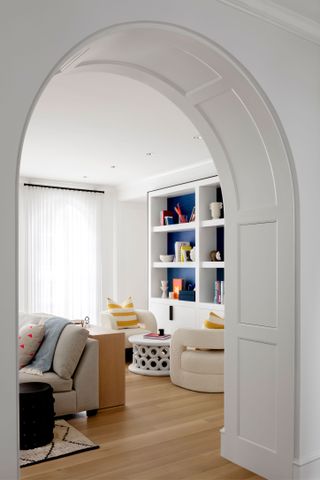 family living room viewed through arched doorway with contemporary club chairs and white display shelves grey sofa