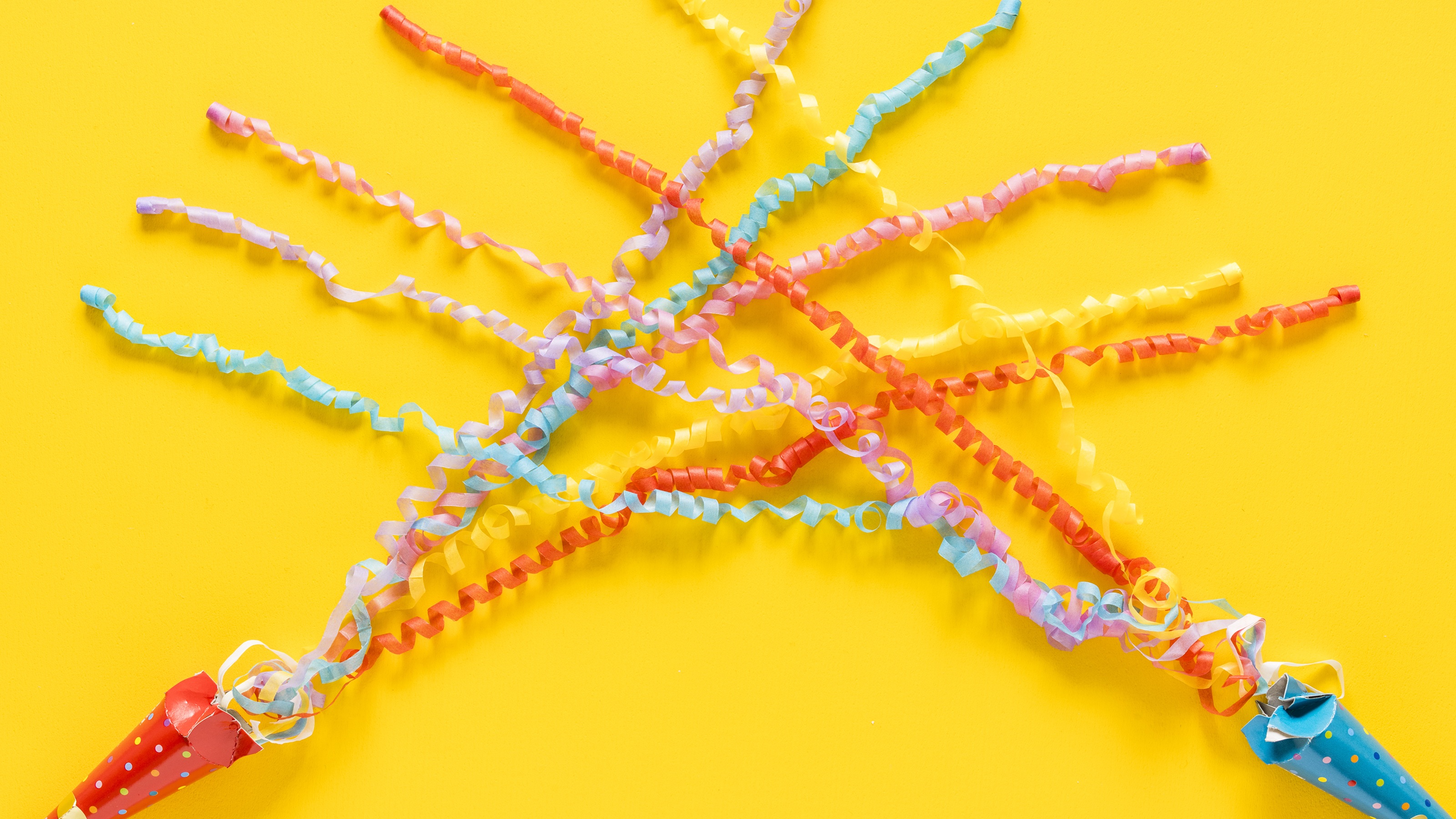 Two party poppers with streamers against a yellow background.