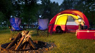 A campsite in the evening with two blue chairs and a campfire