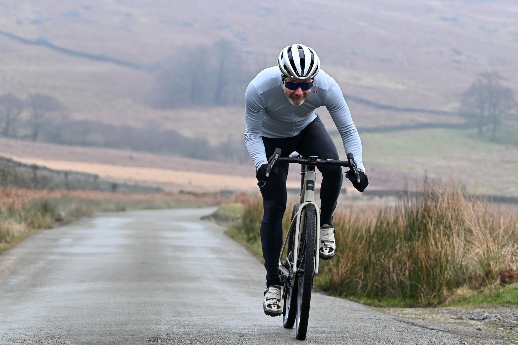 Man in a blue jersey riding a gravel bike on a Peak district lane, out of the saddle