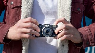 Man holding Pentax Q10 mirrorless camera against a white t-shirt 