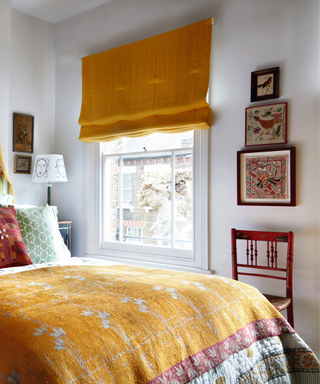 bedroom with yellow bedding and curtain and wall full of artwork and red chair