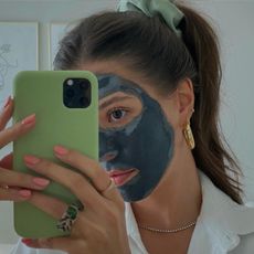 A woman taking a selfie wearing a clay face mask
