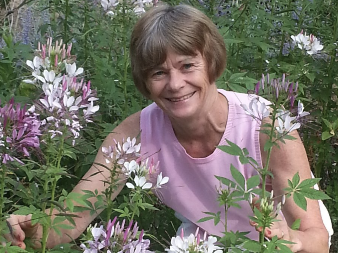 woman with short hair smiling to camera, surrounded by flowers