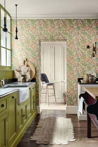 A galley kitchen with cream cabinets, green patterned wallpaper and a pantry