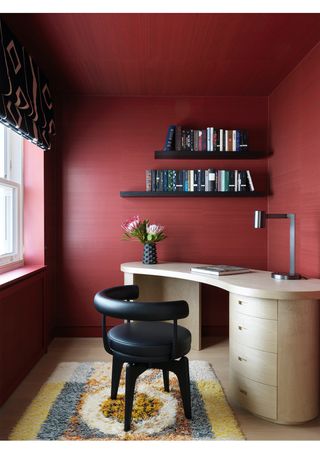 Red home office with wooden desk and black wall shelves