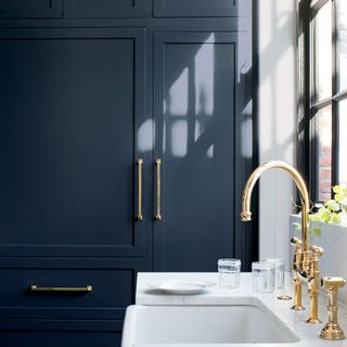 kitchen area with navy blue cabinets with white sink and brass tap