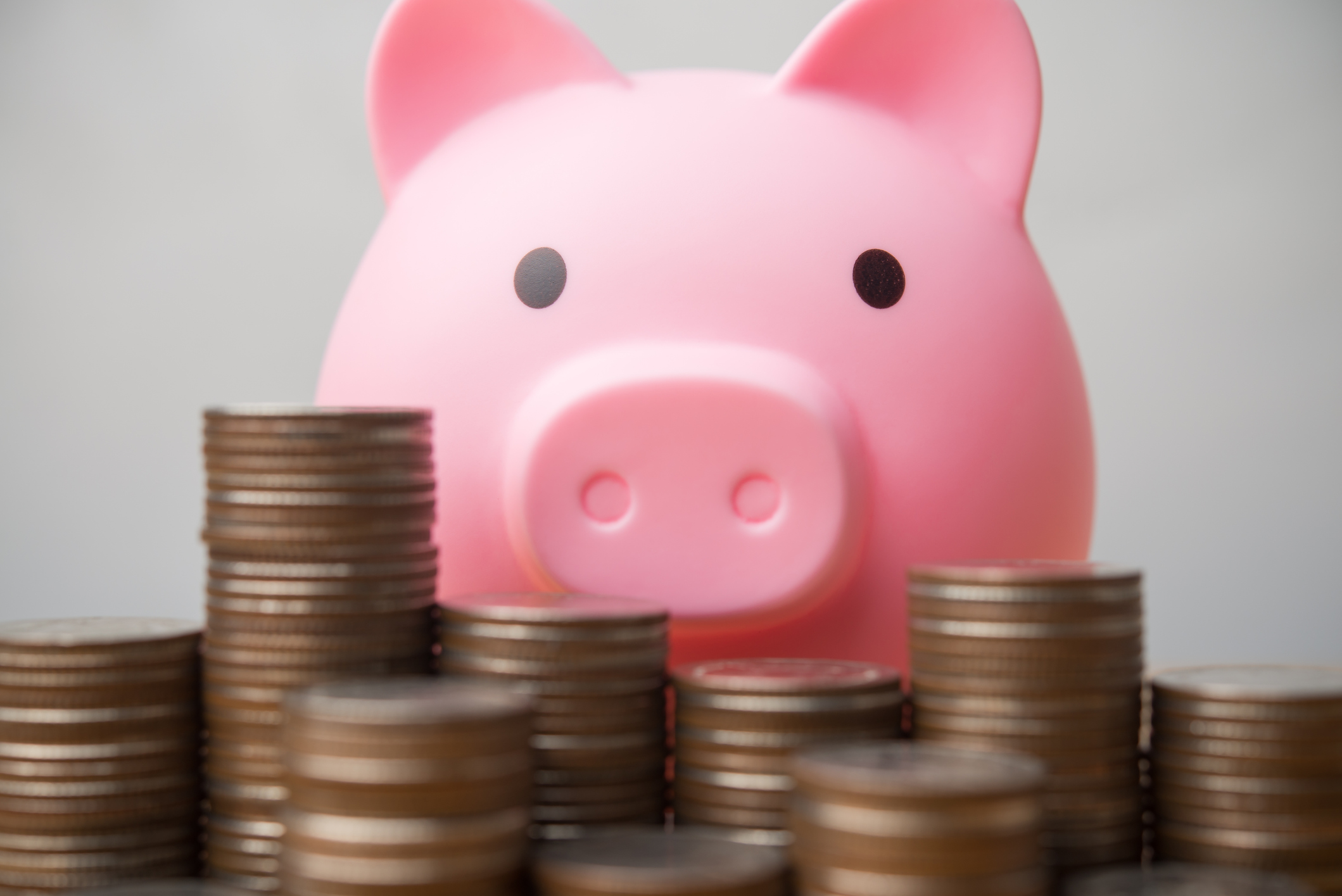 Pink piggy bank with heaps of coins in the foreground.