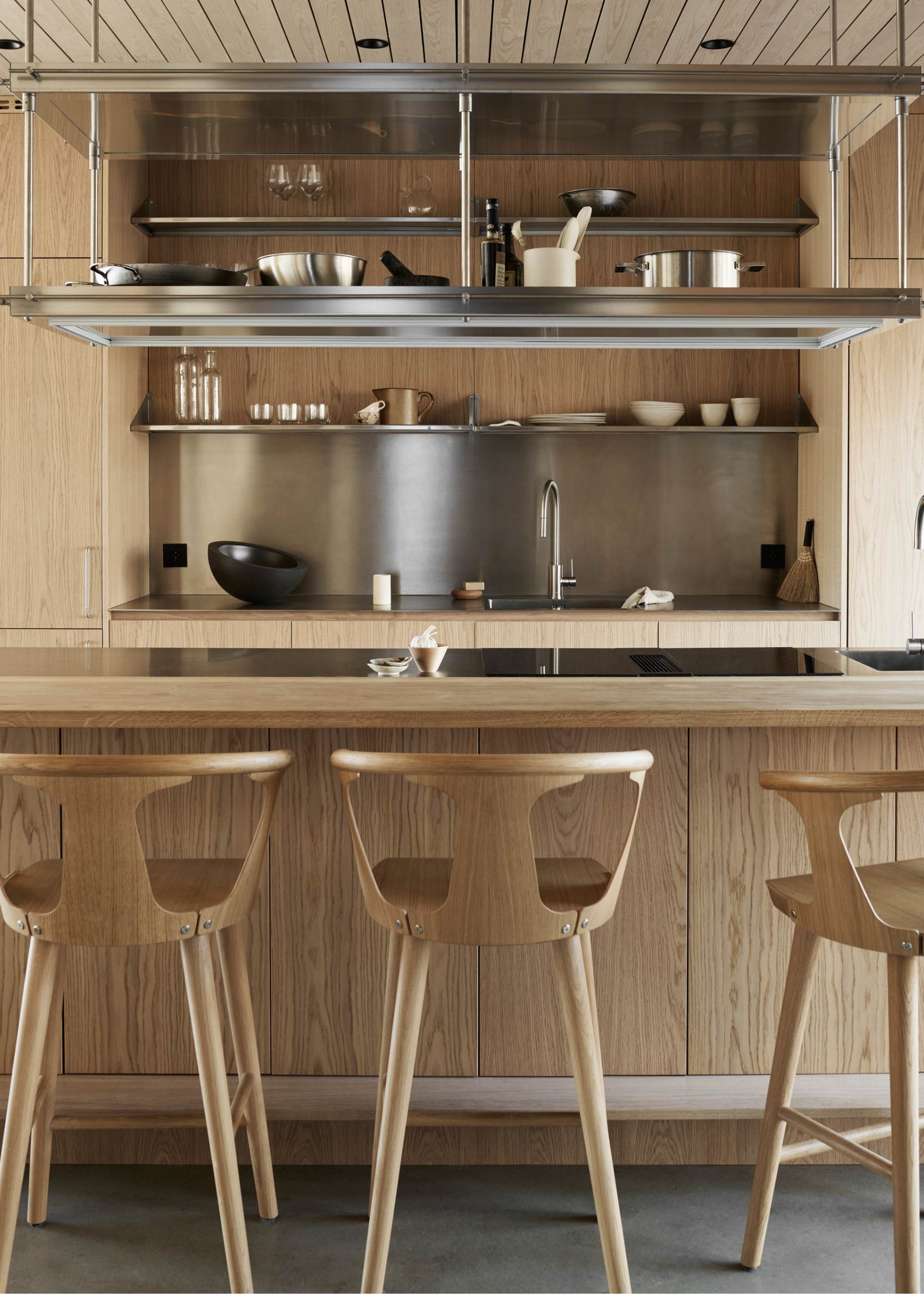 a light oak modern kitchen with a stainless steel splashback and shelving unit