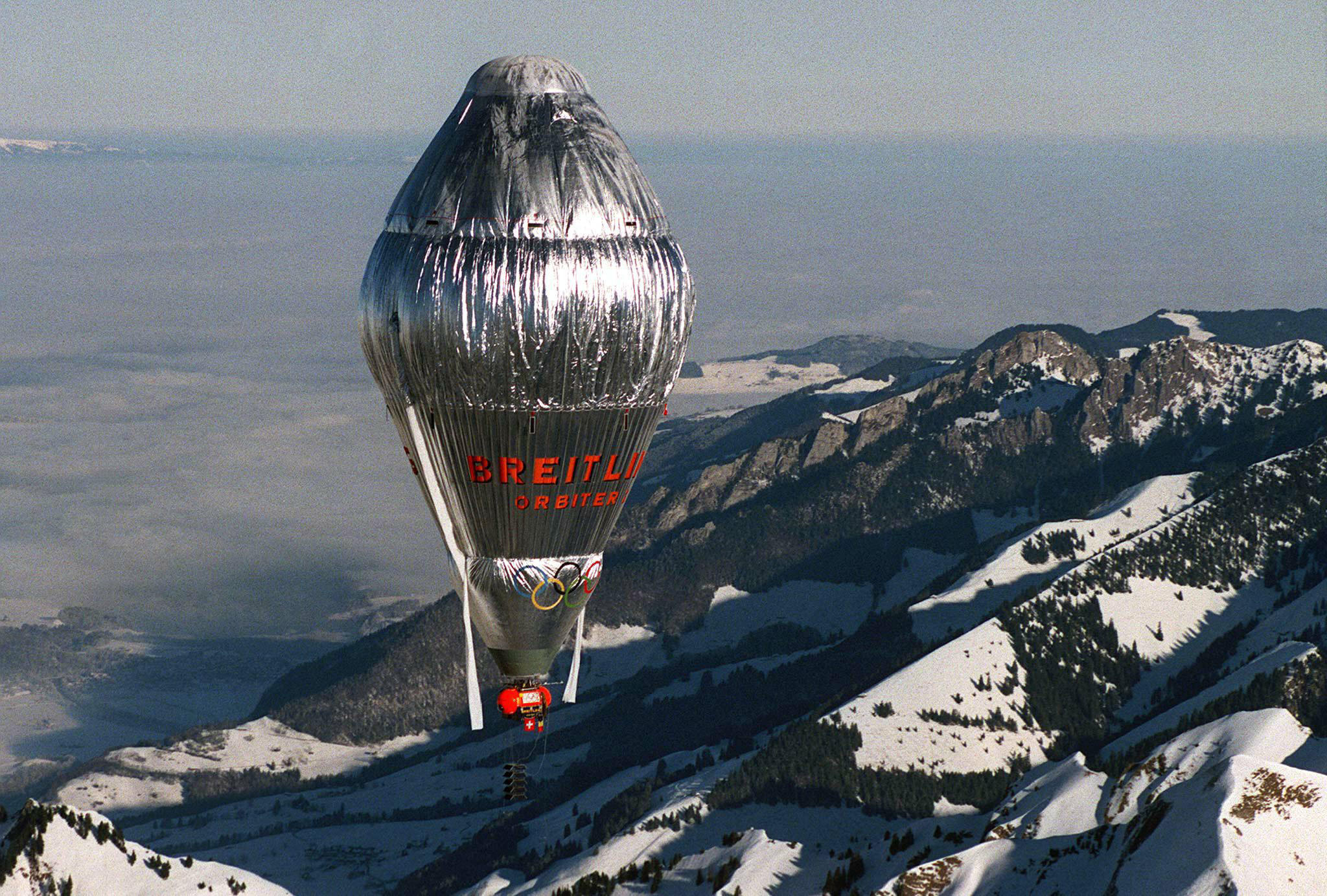 Silver hot air balloon flying over some snowy mountains