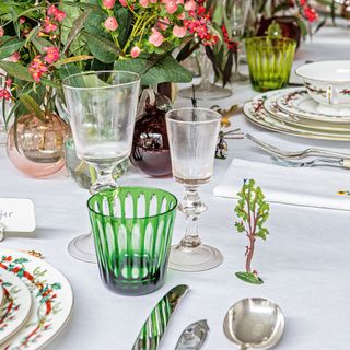 Green and see-through glasses on top of a white table cloth decorated with flowers and cutlery