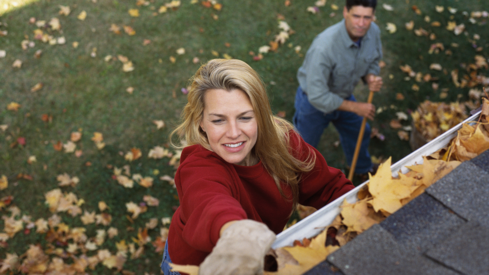 woman cleaning leaves out of gutter with man stood below watching 