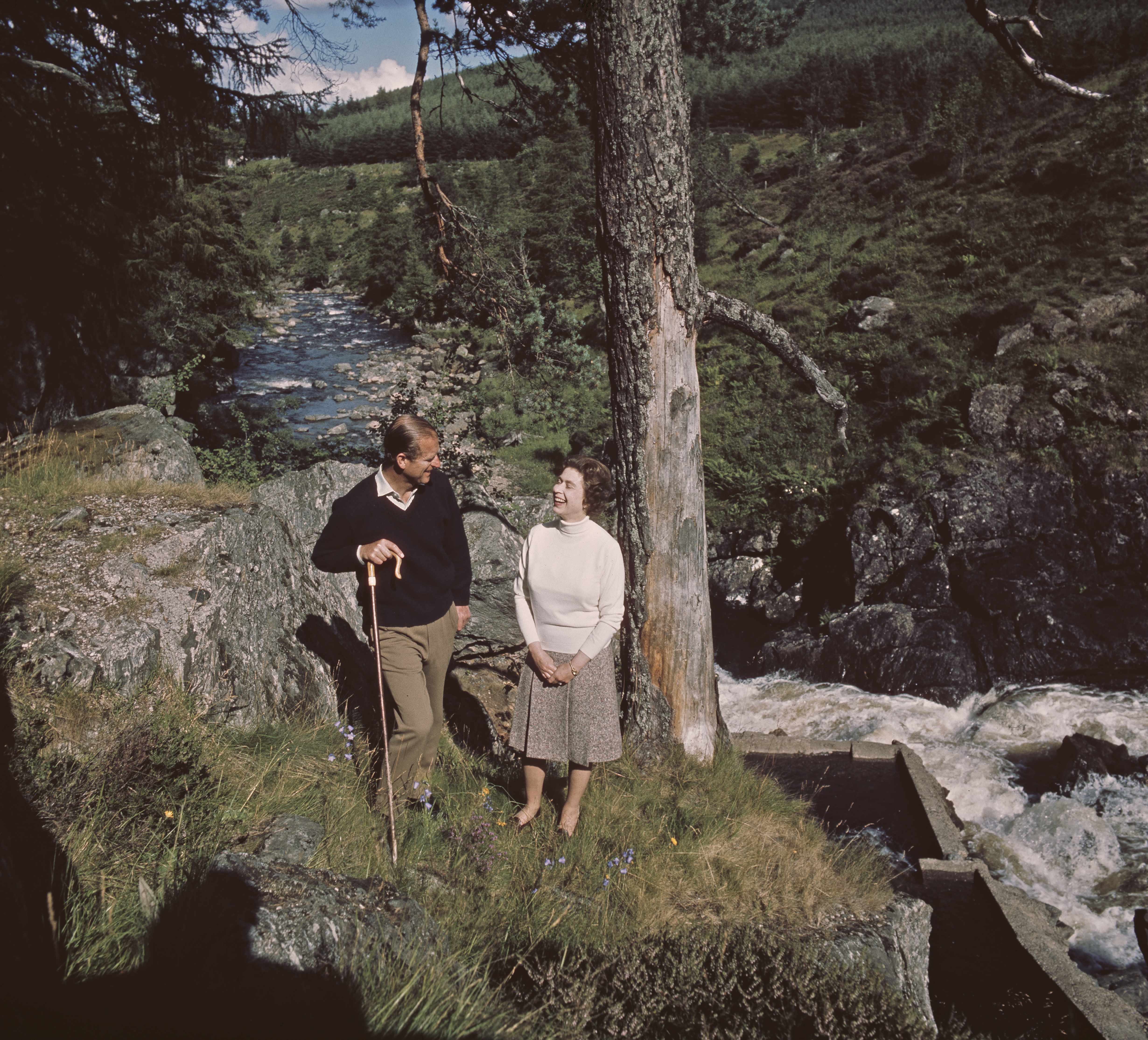 Queen Elizabeth and Prince Philip standing next to a waterfall at Balmoral