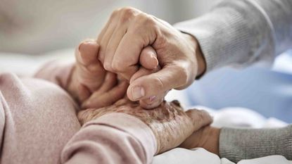 Photo of a caregivers hands grasping elderly hands