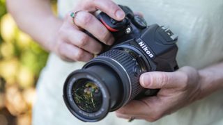 Bästa systemkamera för nybörjare: En person som står utomhus och håller i en Nikon D3500.