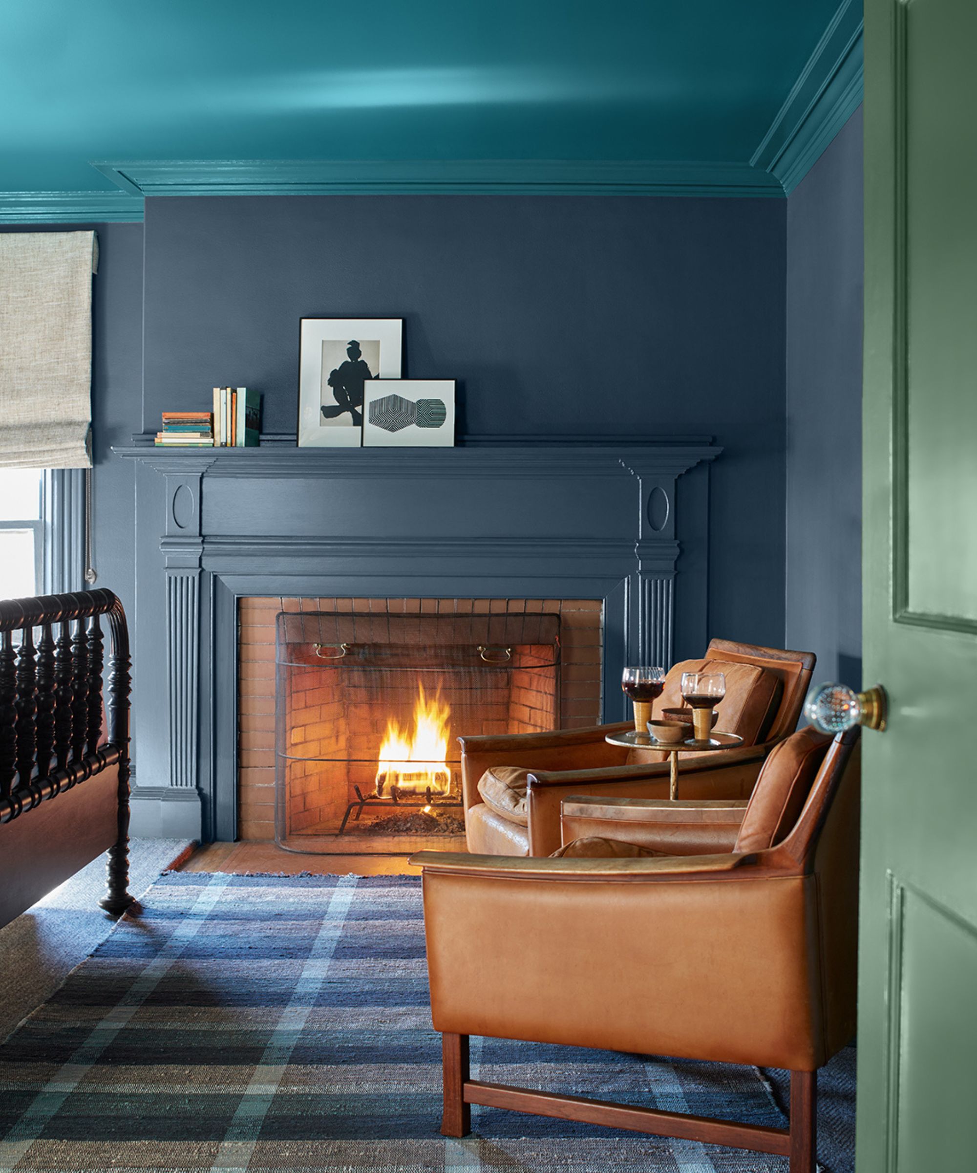 Bedroom with blue painted fireplace, blue plaid rug, brown leather armchairs and green door