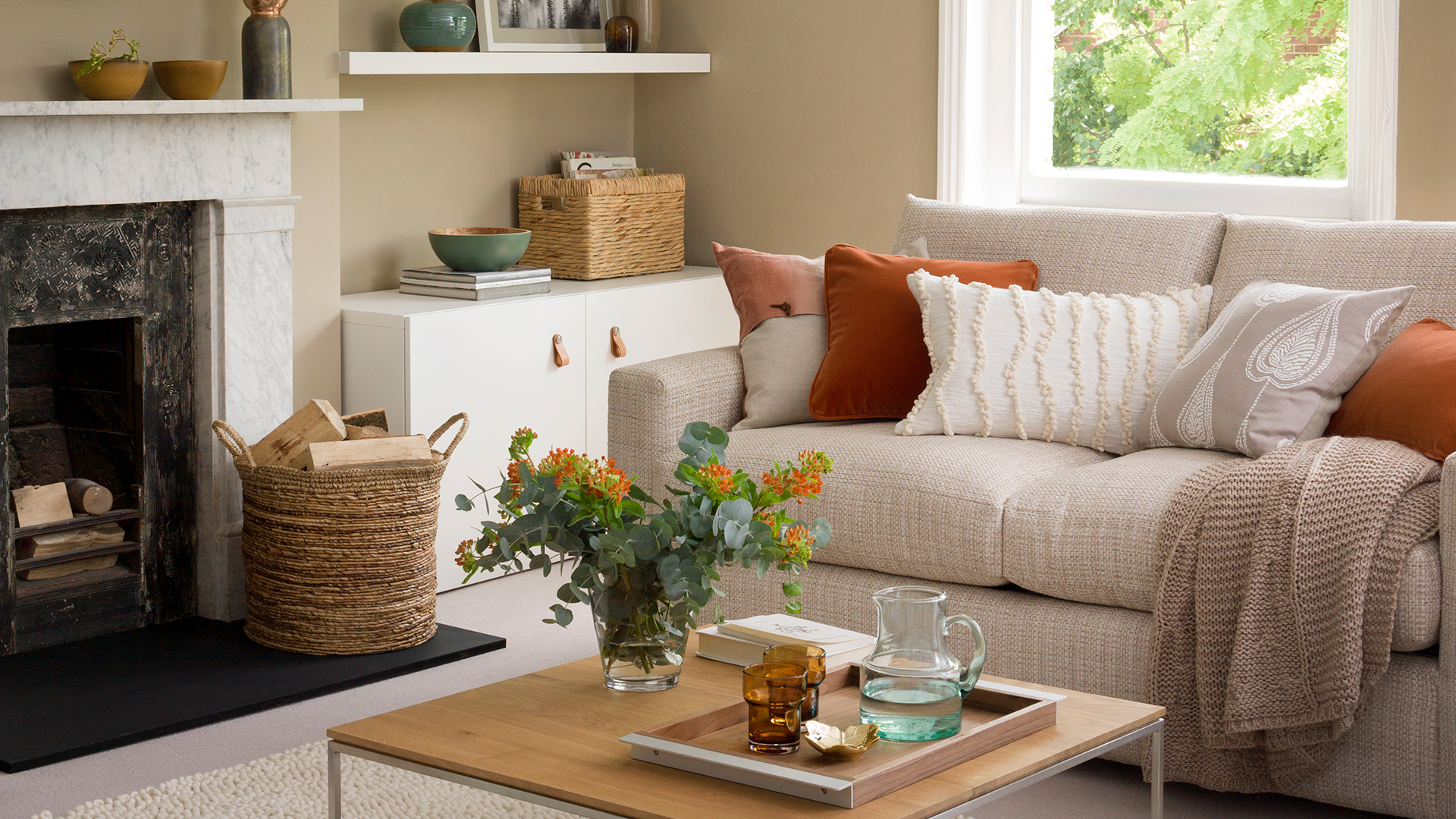 Beige living room with a beige sofa dressed with burnt orange cushions and cosy throws for autumn decor ideas