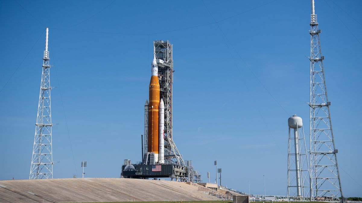 NASA&#039;s Artemis 1 Space Launch System on the launch pad with lightning towers nearby and a blue sky.