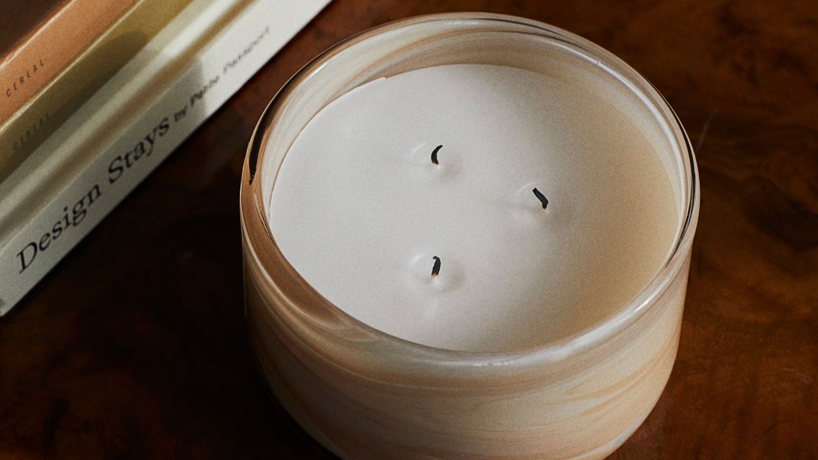 Three-wick candle with cream swirling glass holder on a mahogany coffee table