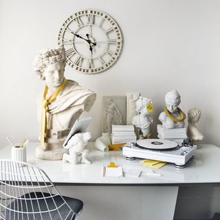 white wall with clock on wall white desk with white statues