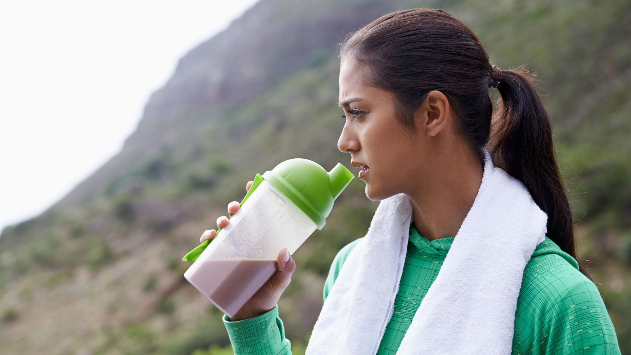 A woman drinking a shake made with one of the best protein powders after outdoor exercise