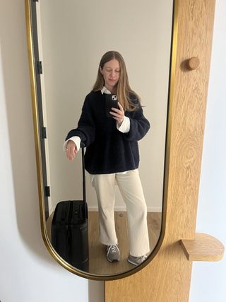 a woman wearing a black sweater and tan pants taking a mirror selfie with a suitcase
