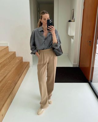 @anoukyve trägt eine beige Hose, ein graues Hemd und beige Turnschuhe