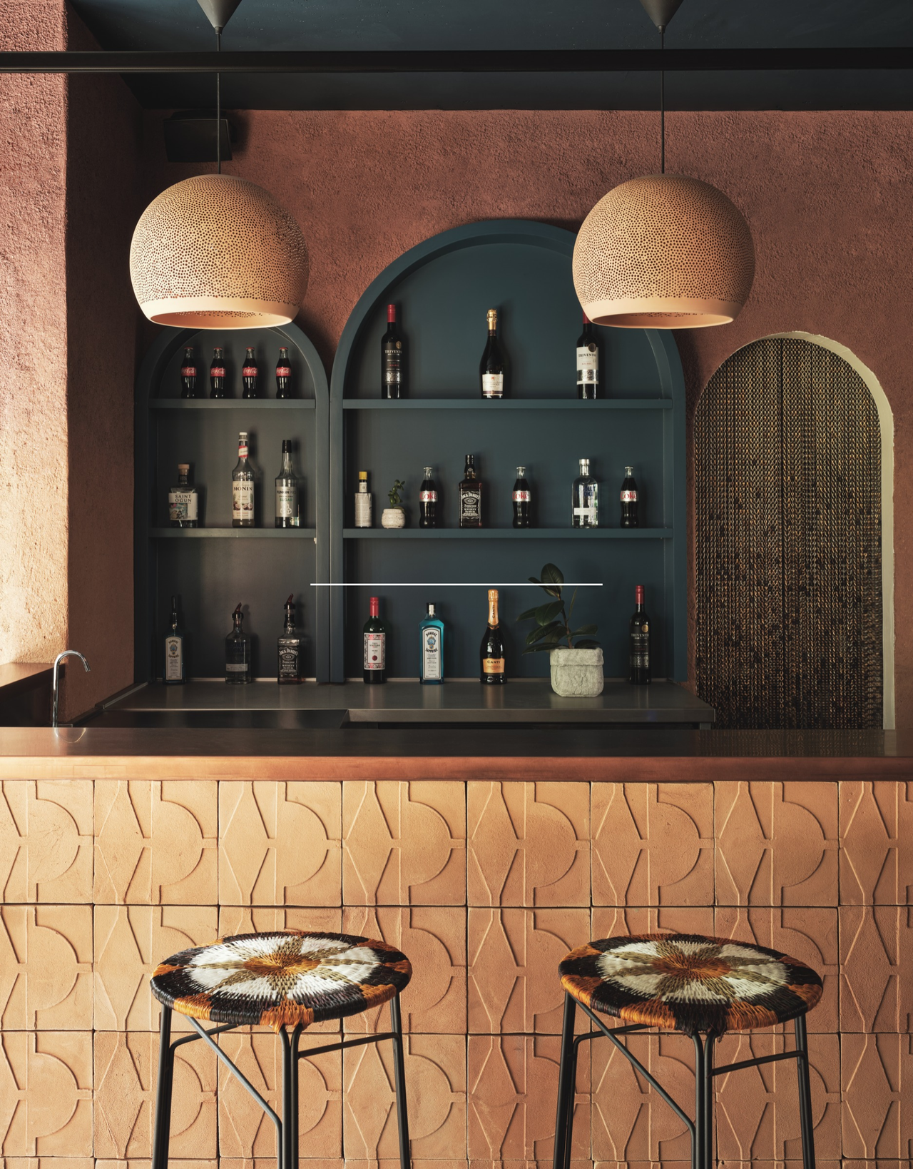 A textured Earthy home bar with arched cabinets, a beaded curtain, a tiled island, and woven seats