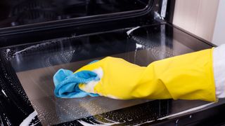 Wiping the inside of an oven door wearing rubber gloves