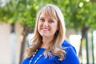 A phot of Dr. Krista Herrera standing outside. She is wearing a blue outfit and has blond hair that falls below her shoulders.