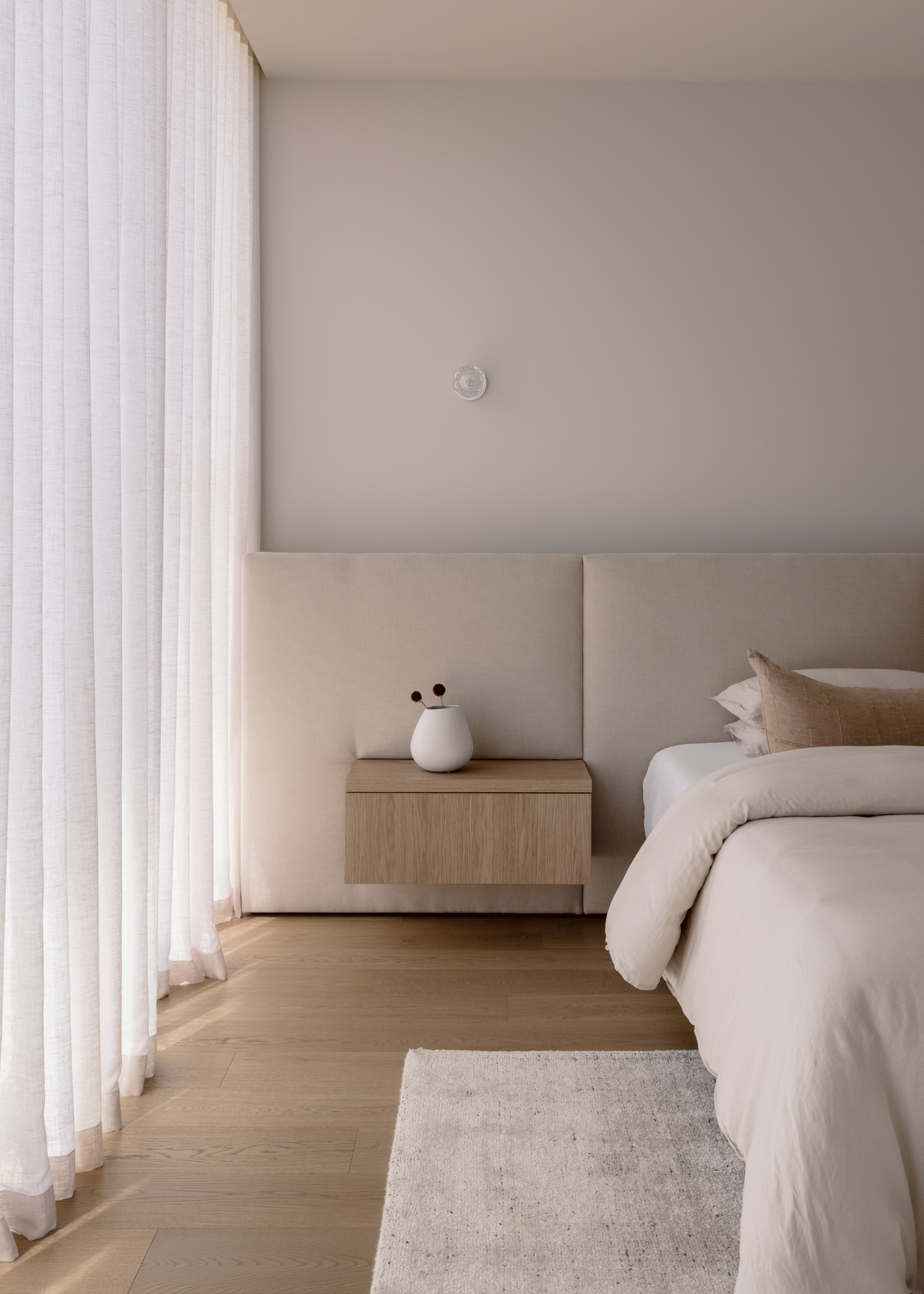 A floating nightstand on an extended headboard by a minimalist bed