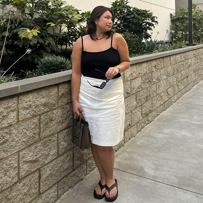 Marina wears black tank top, white linen skirt, and black flip flops while posing for a picture. 