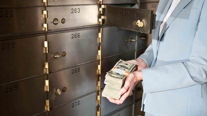 Businesswoman holding big stack of US paper currency, standing by safety deposit boxes