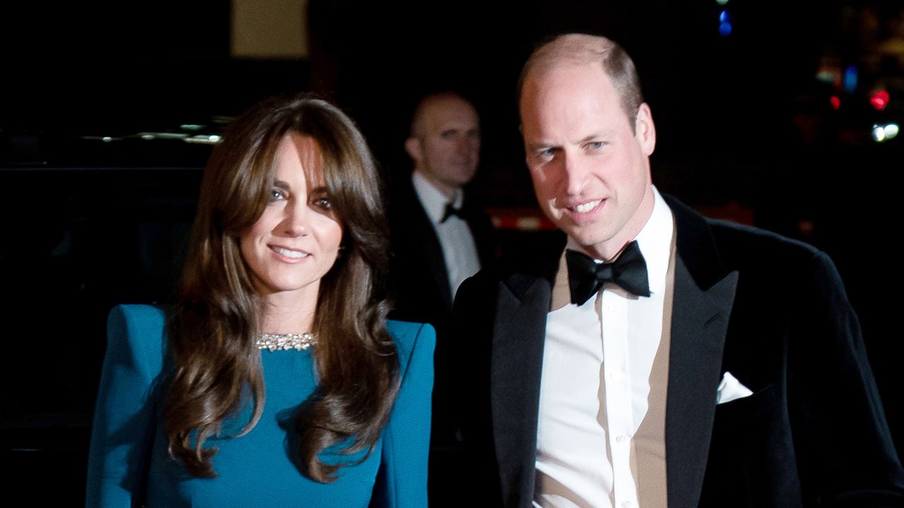 Kate Middleton wears a teal dress and has long brunette hair and bangs, Prince William wears a tuxedo