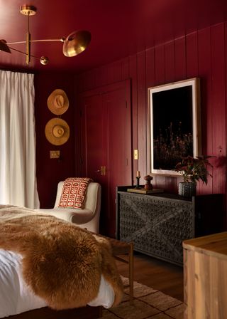 bedroom color drenched in deep red color with fur throw, brass pendant light and artwork