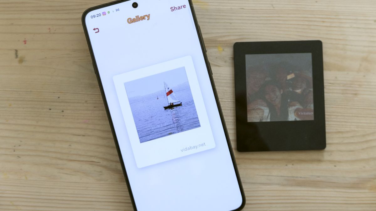 Vidabay Snap E Ink Polaroid-like frame laid on a table alongside a smartphone with the Vidabay app on display