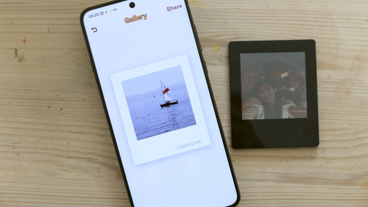 Vidabay Snap E Ink Polaroid-like frame laid on a table alongside a smartphone with the Vidabay app on display