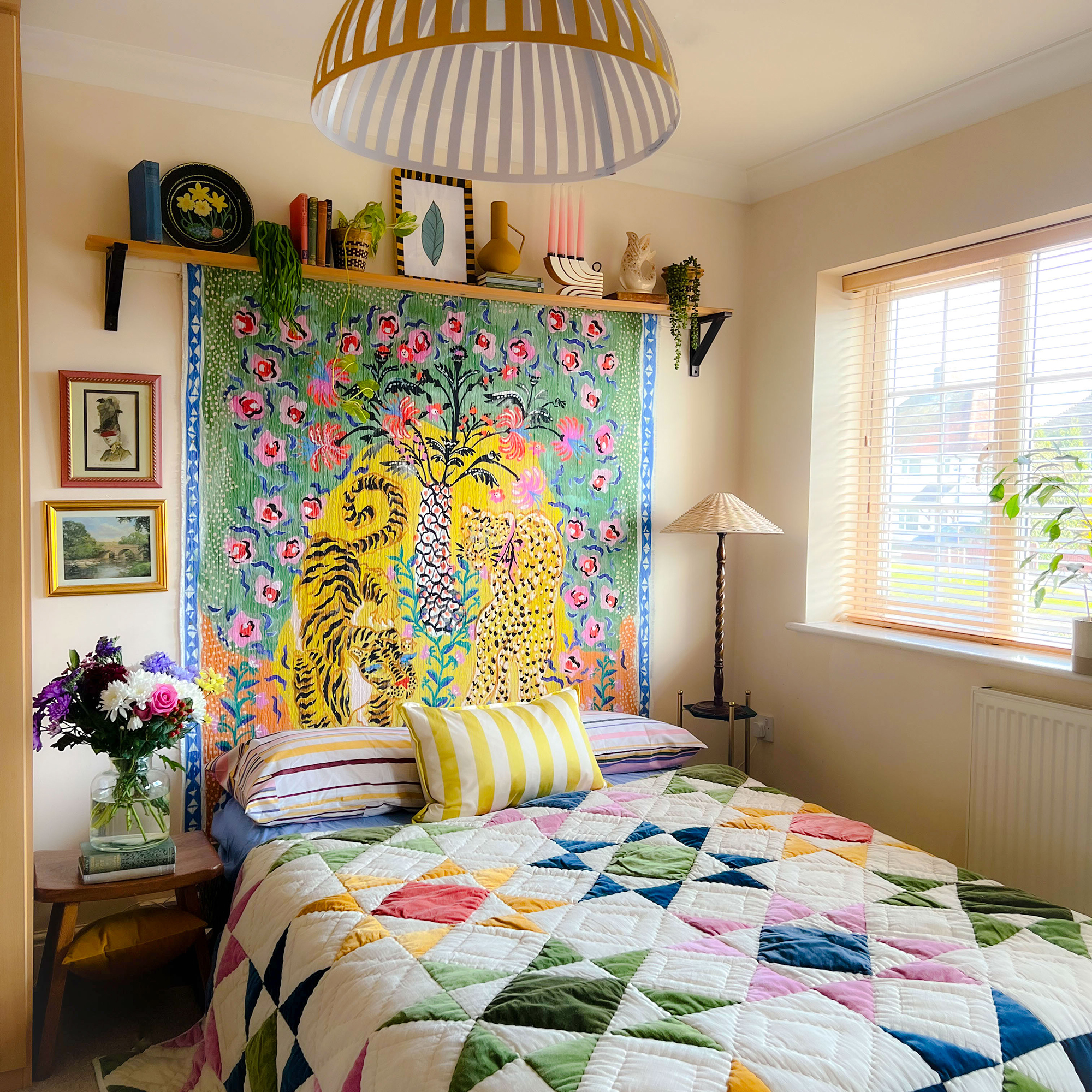 Small beige bedroom with a bed dressed with a colourful patchwork quilt and a throw hung on the wall in the space between the bed and a shelf