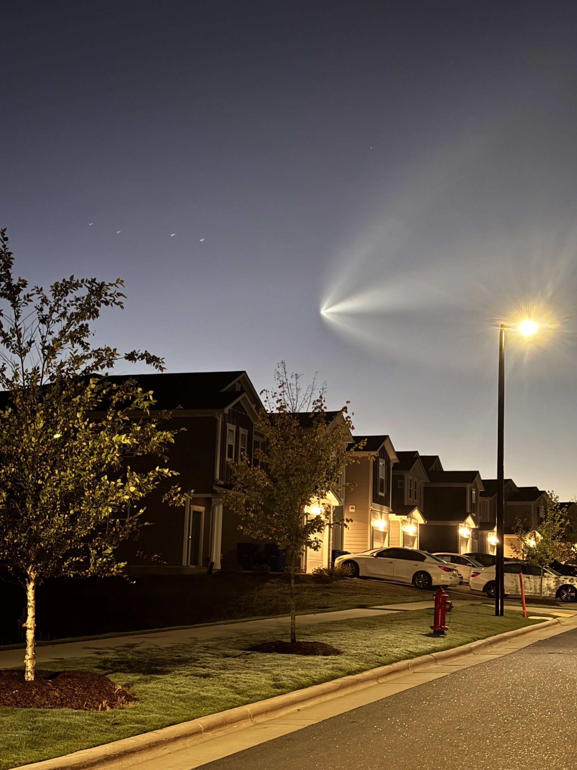 a bright array flies in the sky above a street lamp-lit row of homes.