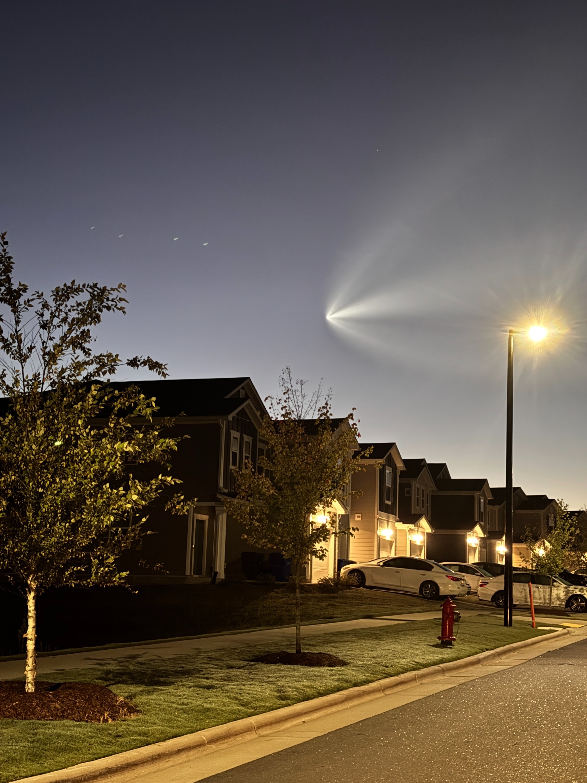 a bright array flies in the sky above a street lamp-lit row of homes.