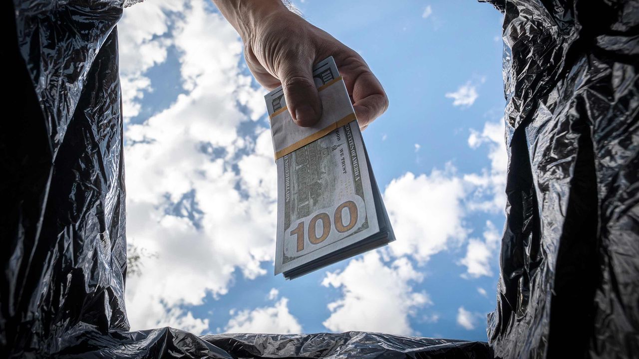 A man throws away a bundle of $100 bills into a garbage bag.