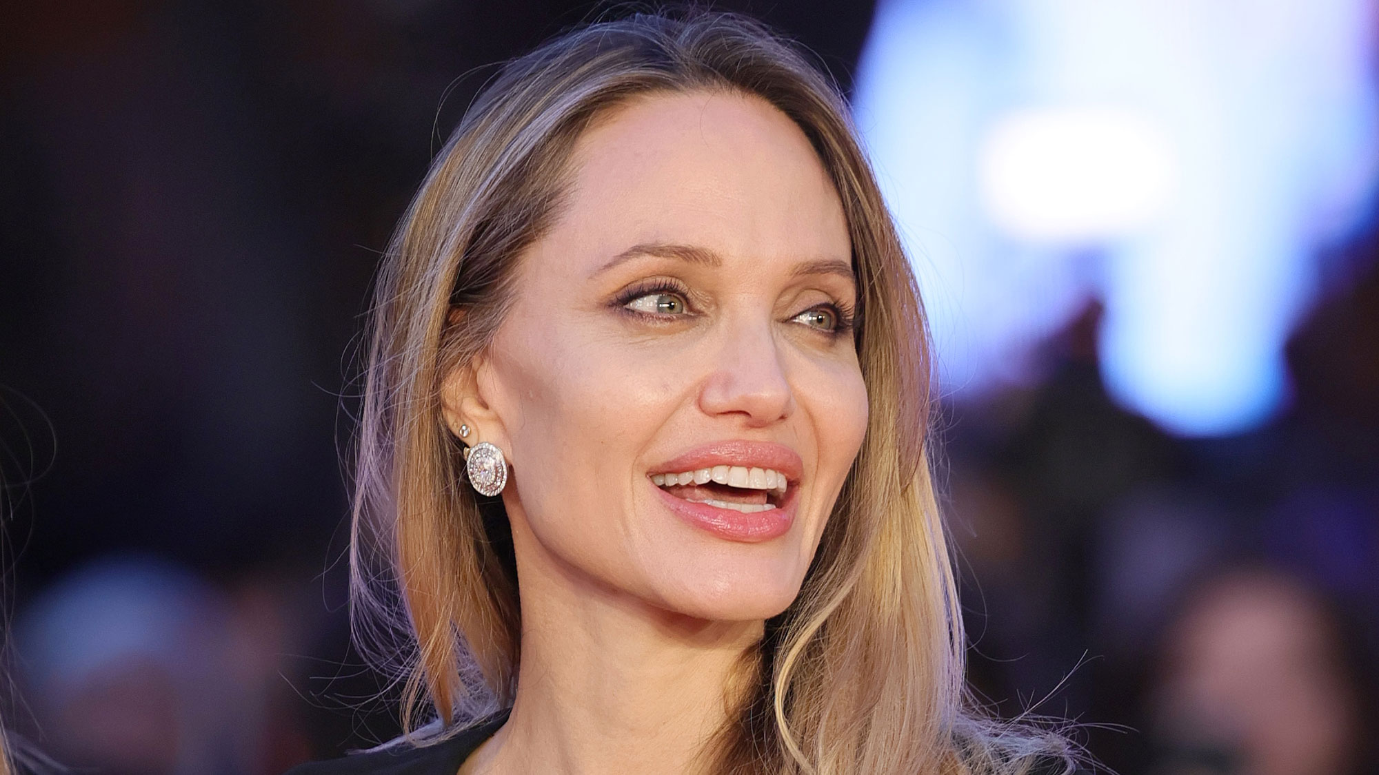 Angelina Jolie smiles wearing a black dress on the red carpet.