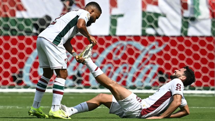A soccer player helps a teammate on the ground with a muscle cramp