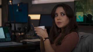 Aubrey Plaza holds a cup of coffee while sitting near her computer in Operation Fortune: Ruse de Guerre.