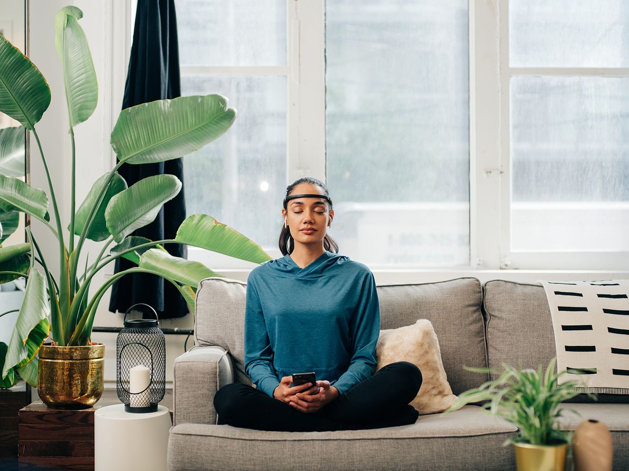 woman wearing Muse 2 headset on a grey couch surrounded by plants