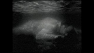Black and white image of a man in white clothing laying face down under water