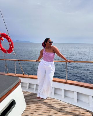 Woman on boat wears striped swimsuit and white linen trousers